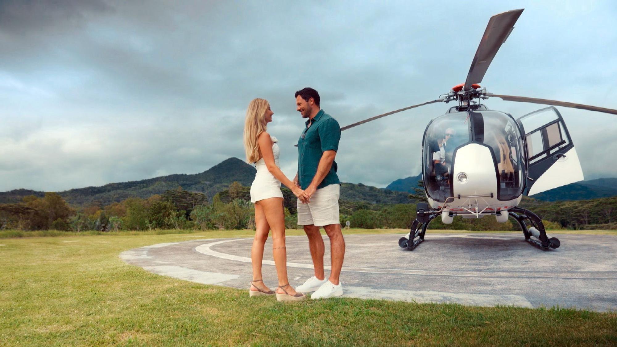 Eine Frau und ein Mann stehen Hand in Hand vor einem Helikopter.