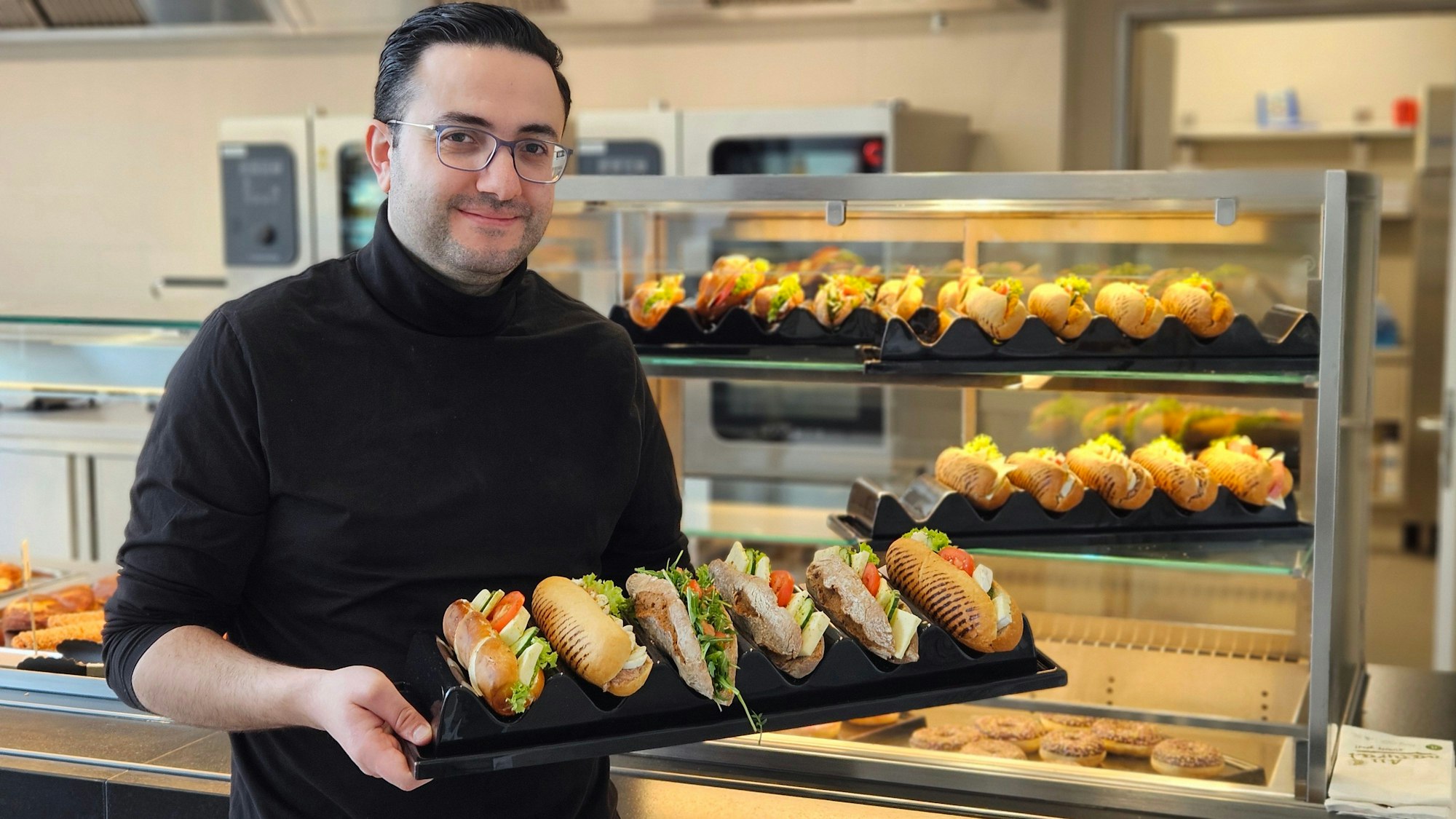 Ein Mann hält ein Tablett mit mehreren belegten Baguettes.