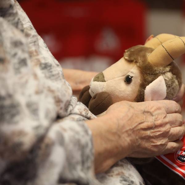 Eine ältere Frau hält einen Stoff-Hennes auf ihrem Schoß.
