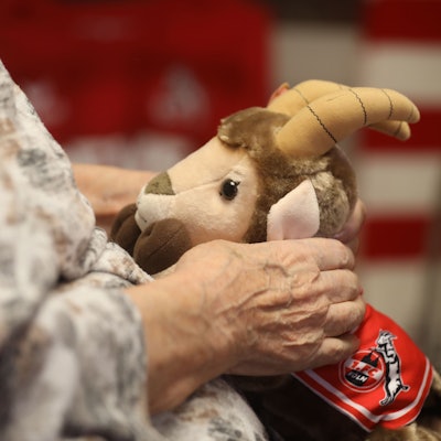 Eine ältere Frau hält einen Stoff-Hennes auf ihrem Schoß.