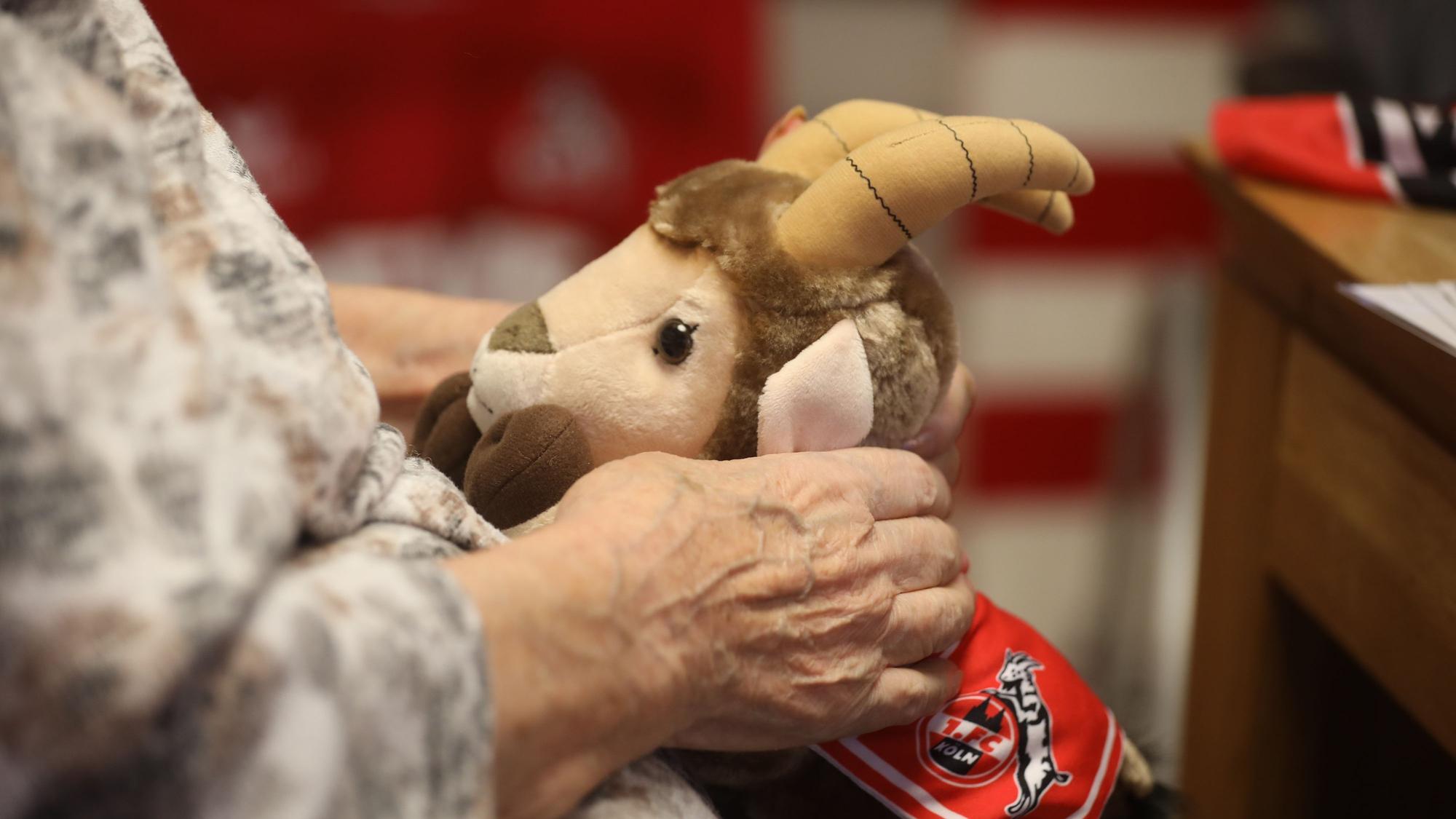 Eine ältere Frau hält einen Stoff-Hennes auf ihrem Schoß.