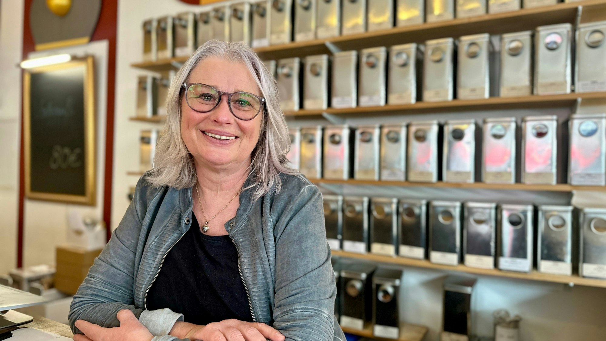 Eine Frau mit schulterlangem Haar und Brille schaut lachend in die Kamera.