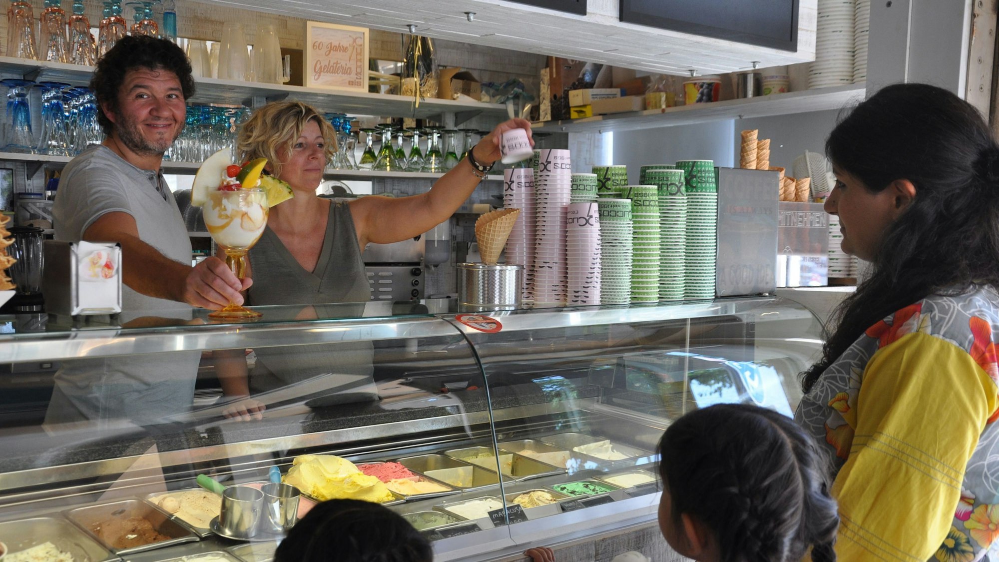 Seit Jahrzehnten versorgen Lorenzo Cucco und Nicoletta Bez Elsdorf mit Speiseeis. Hier stehen sie hinter der Eistheke, eine Frau mit Kindern wird bedient.