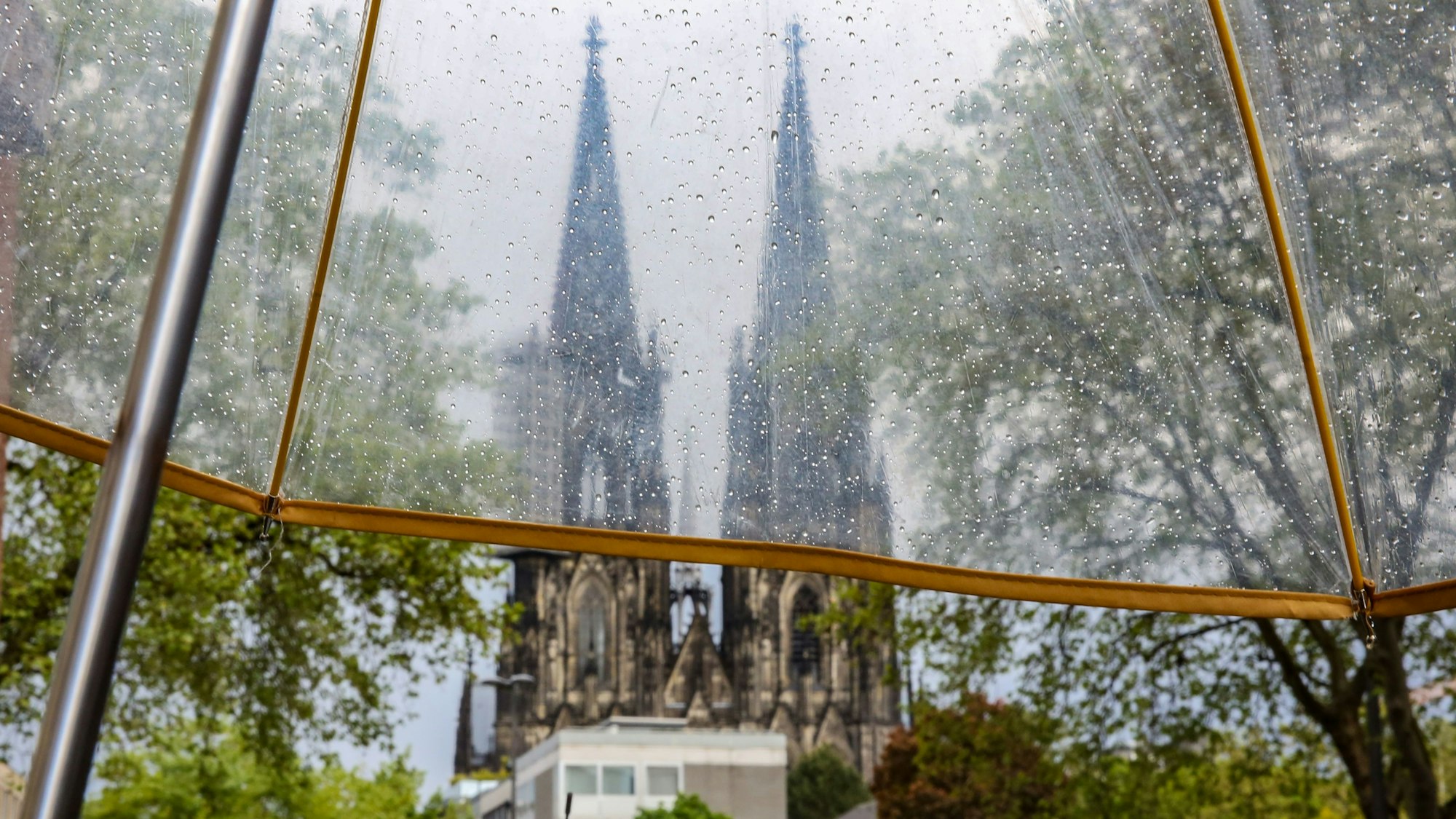 Regenwetter in Köln, Blick auf den Kölner Dom durch einen durchsichtigen Regenschirm.