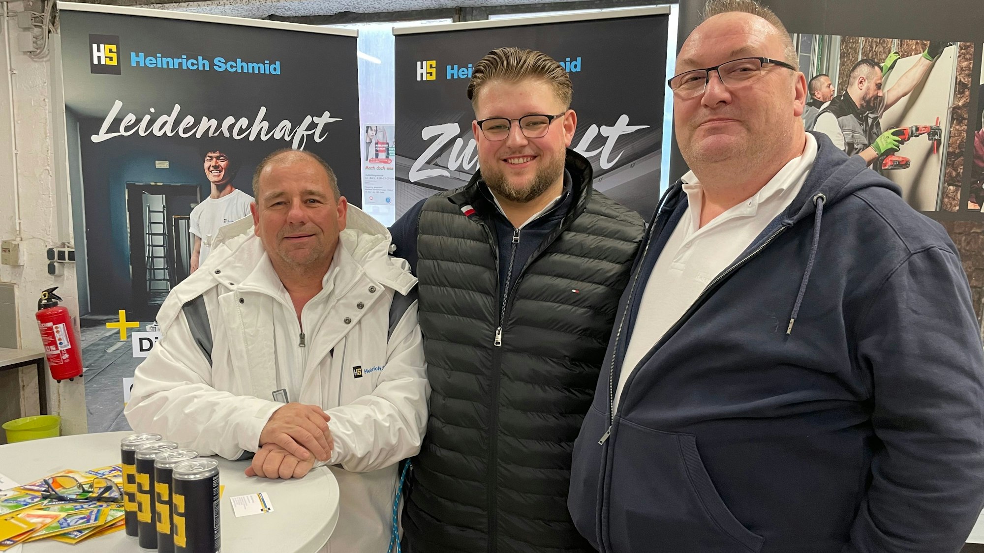 Drei Männer stehen an einem Stehtisch vor Roll-ups.