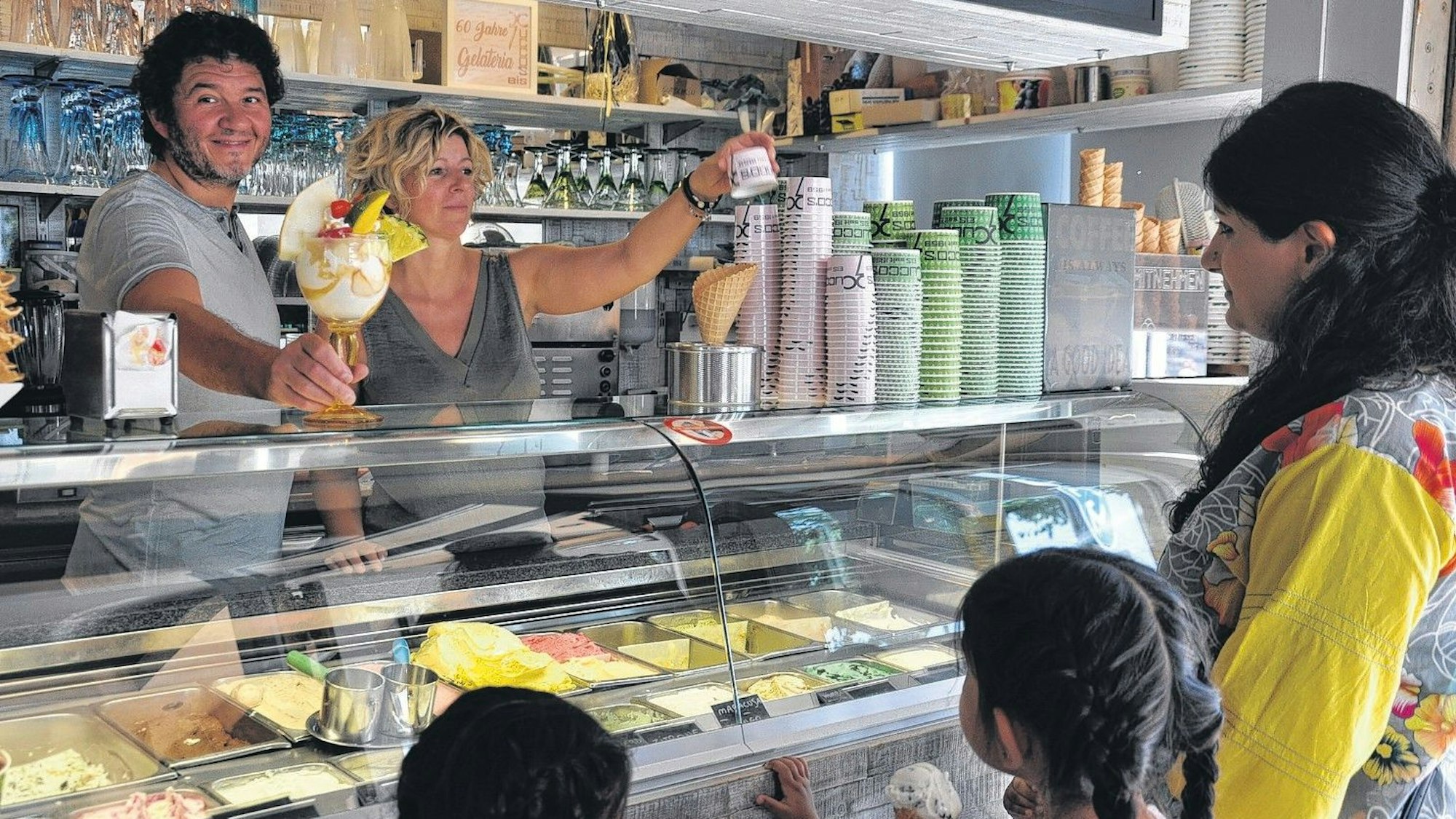 Seit Jahrzehnten versorgen Lorenzo Cucco und Nicoletta Bez Elsdorf mit Speiseeis. Hier stehen sie hinter der Eistheke, eine Frau mit Kindern wird bedient.