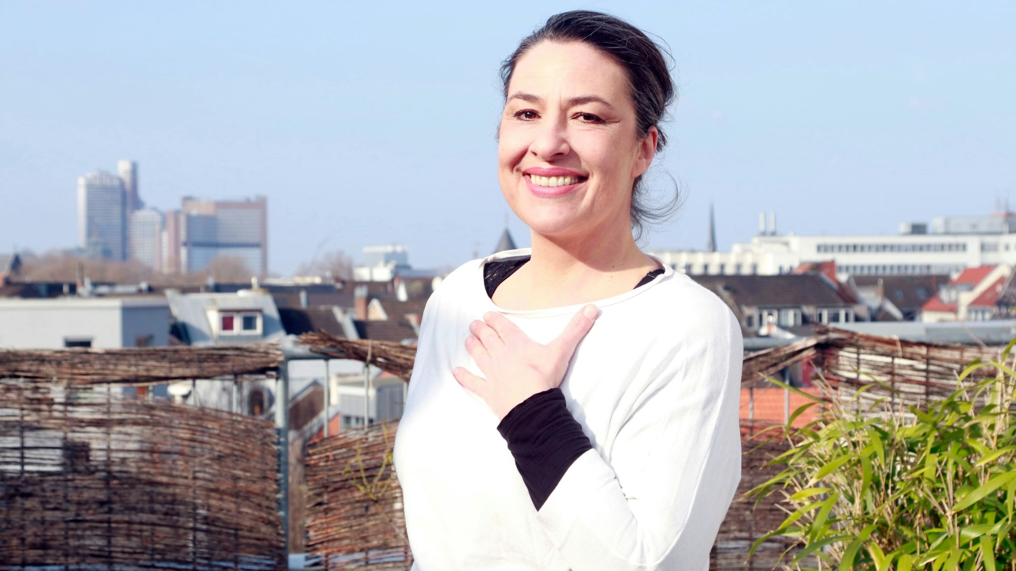 Eine Frau steht auf einem Balkon und blickt in die Kamera.