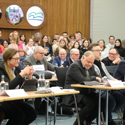 Die Politiker und Politikerinnen von Grünen und CDU sitzen im Kreistag im Kreishaus des Rheinisch-Bergischen Kreises an Tischen. Im Hintergrund sind Zuschauerinnen und Zuschauer zu sehen.