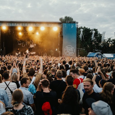 Menschen stehen vor einer Open-Air-Bühne.