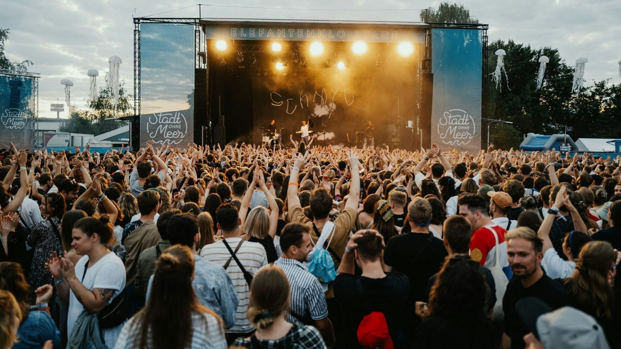 Menschen stehen vor einer Open-Air-Bühne.