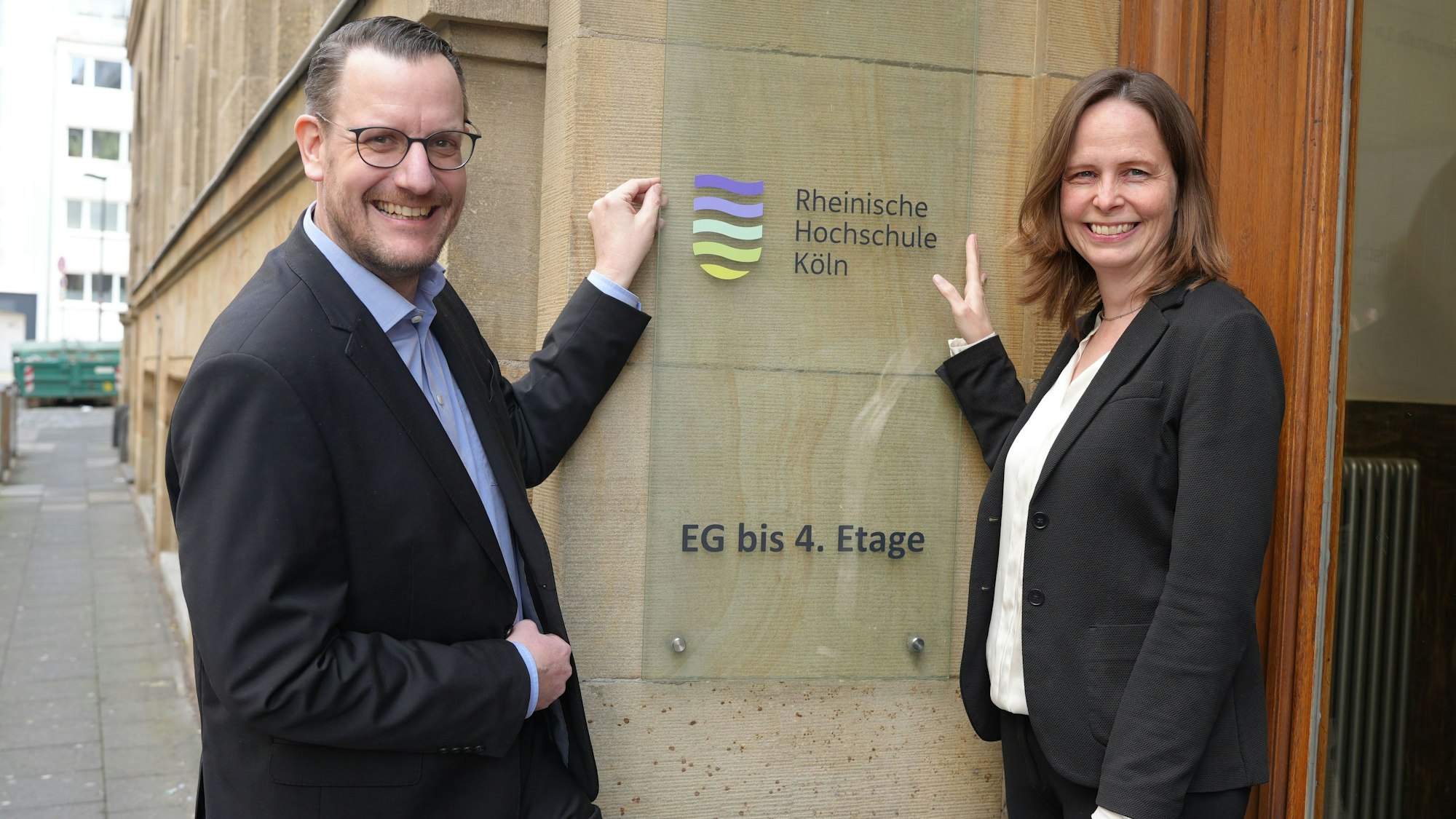 Martin Topp, Geschäftsführer und Kanzler, und Präsidentin Claudia Bornemeyer zeigen auf das neue Logo der umbenannten Rheinischen Hochschule