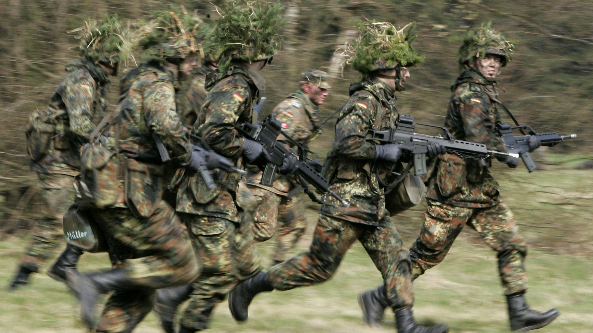 Mit Blattwerk und Gras getarnte Soldaten rennen bei einer Übung über eine Wiese.