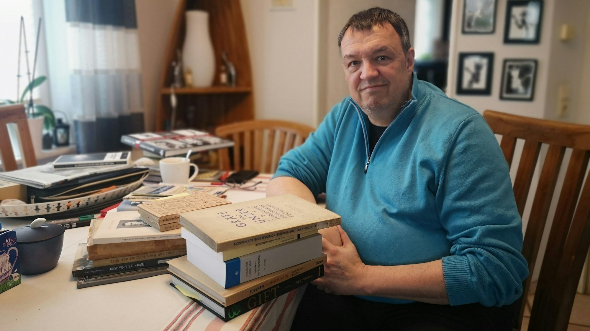 Autor Ralf Thiesen an seinem Arbeitsplatz in seinem Haus. Sein Tisch ist voll beladen mit Fachbüchern, die er für die Recherche seines Romans genutzt hat.