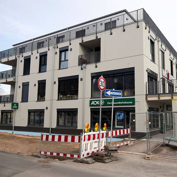 In einen Neubau am Kaller Bahnhof ist die Krankenkasse AOK eingezogen, das Banner ist über dem Eingang im Erdgeschoss zu sehen. Vor dem Haus ist noch eine Baustelle.