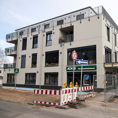 In einen Neubau am Kaller Bahnhof ist die Krankenkasse AOK eingezogen, das Banner ist über dem Eingang im Erdgeschoss zu sehen. Vor dem Haus ist noch eine Baustelle.