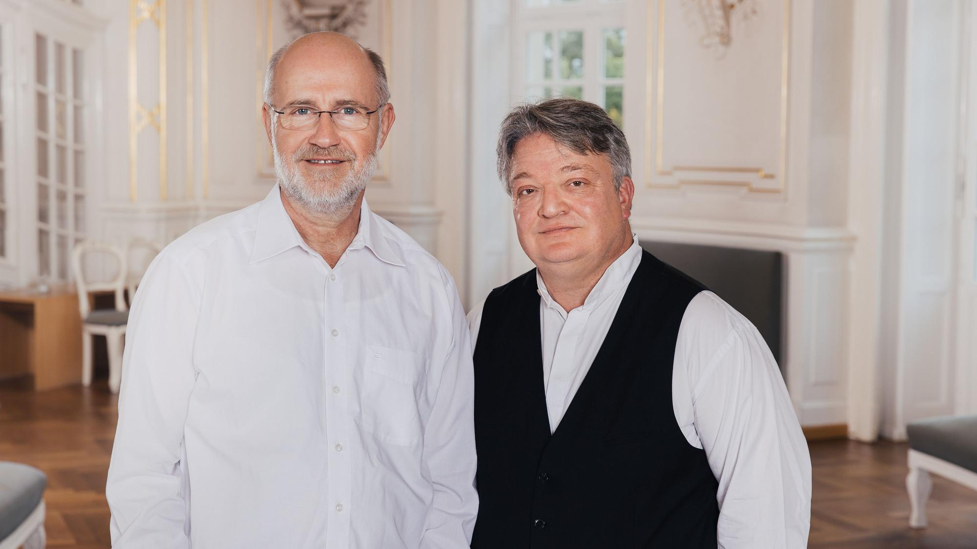 Harald Lesch (l.), in weißem Hemd, und Martin Walch, mit weißem Hemd und schwarzer Weste, schauen in die Kamera.