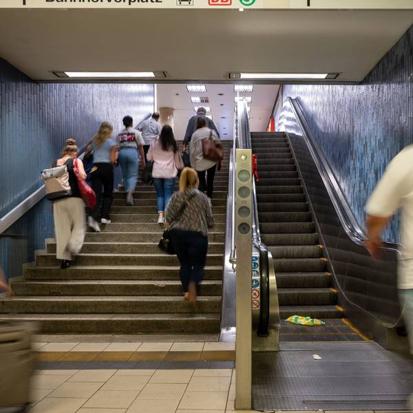 Menschen steigen eine Treppe an der KVB-Haltestelle Dom/Hauptbahnhof hoch, ein Mann geht auf die Rolltreppe zu.
