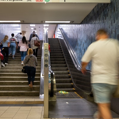 Menschen steigen eine Treppe an der KVB-Haltestelle Dom/Hauptbahnhof hoch, ein Mann geht auf die Rolltreppe zu.