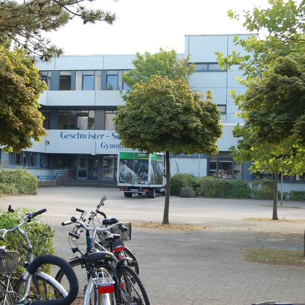 Zu sehen ist ein Schulgebäude mit einer Fassade, auf dem Schulhof stehen Fahrräder.