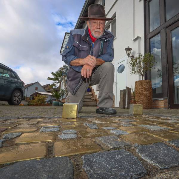 Künstler Gunter Demnig arbeitet goldene Stolpersteine in das Pflaster einer Straße ein.