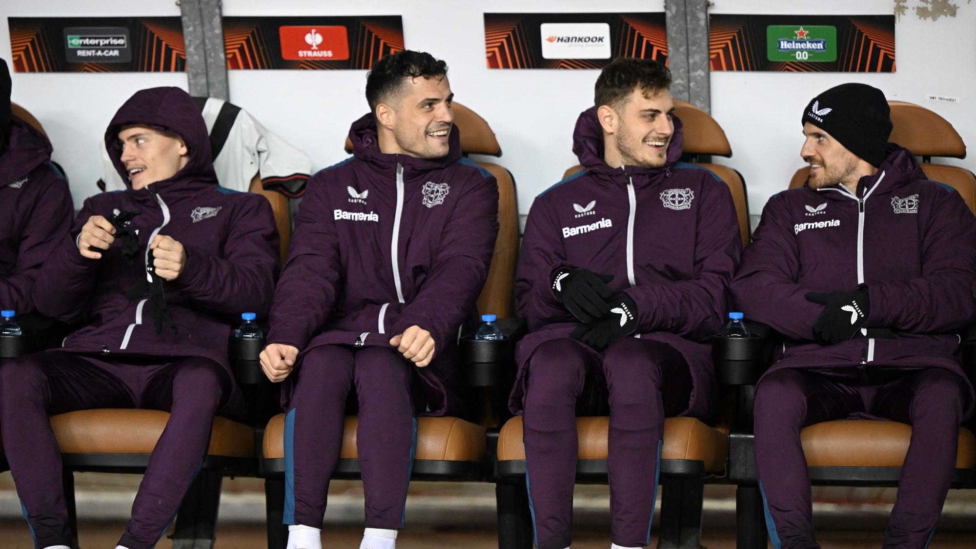Leverkusens Florian Wirtz (l-r), Josip Stanisic, Granit Xhaka und Jonas Hofmann sitzen auf der Bank.