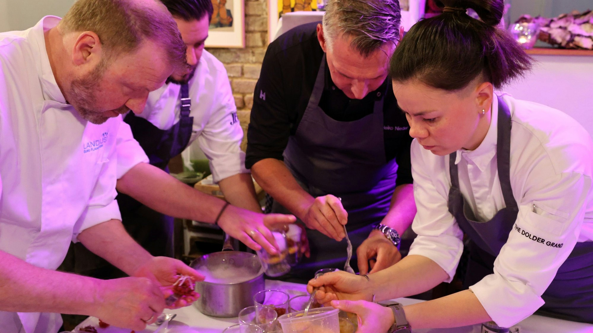 Die drei Köche und die Köchin stehen im Halbkreis und richten Teller mit dem Gruß aus der Küche an.