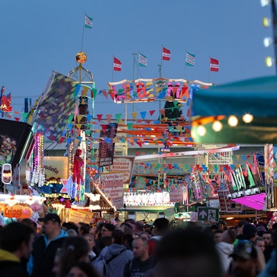 Menschen sind zwischen Kirmesbuden und Fahrgeschäften zu sehen.