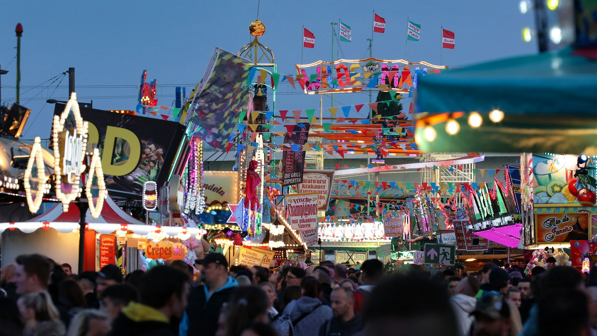 Menschen sind zwischen Kirmesbuden und Fahrgeschäften zu sehen.