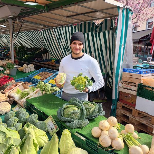 Mann an einem Marktstand mit Gemüse in der Hand