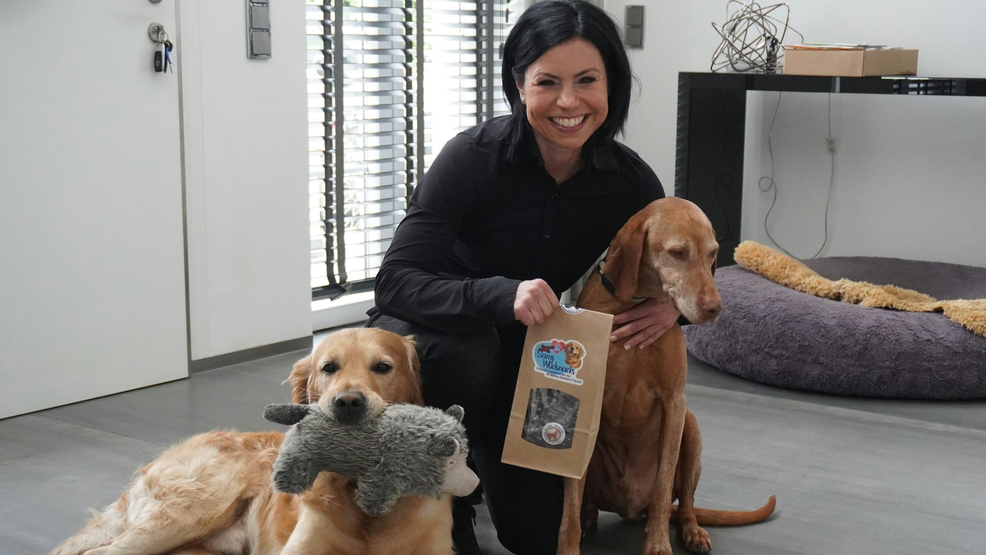 Ein Frau kniet lächelnd neben zwei Hunden.