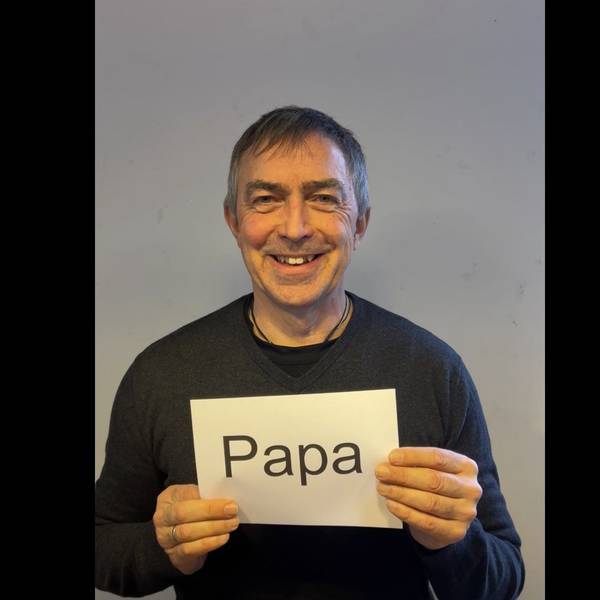 Der Vater hält einen Zettel vor der Brust mit dem Schriftzug „Papa“.