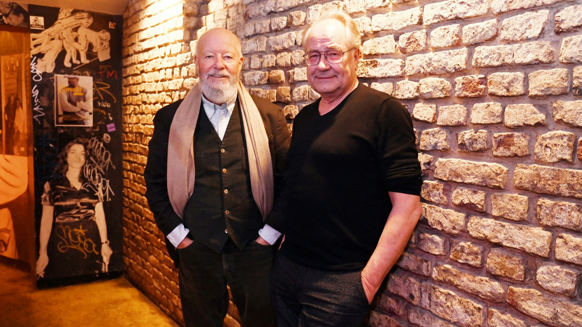 Bill Mockridge und Hartmut Volle lehnen nebeneinander an einer Backsteinwand.