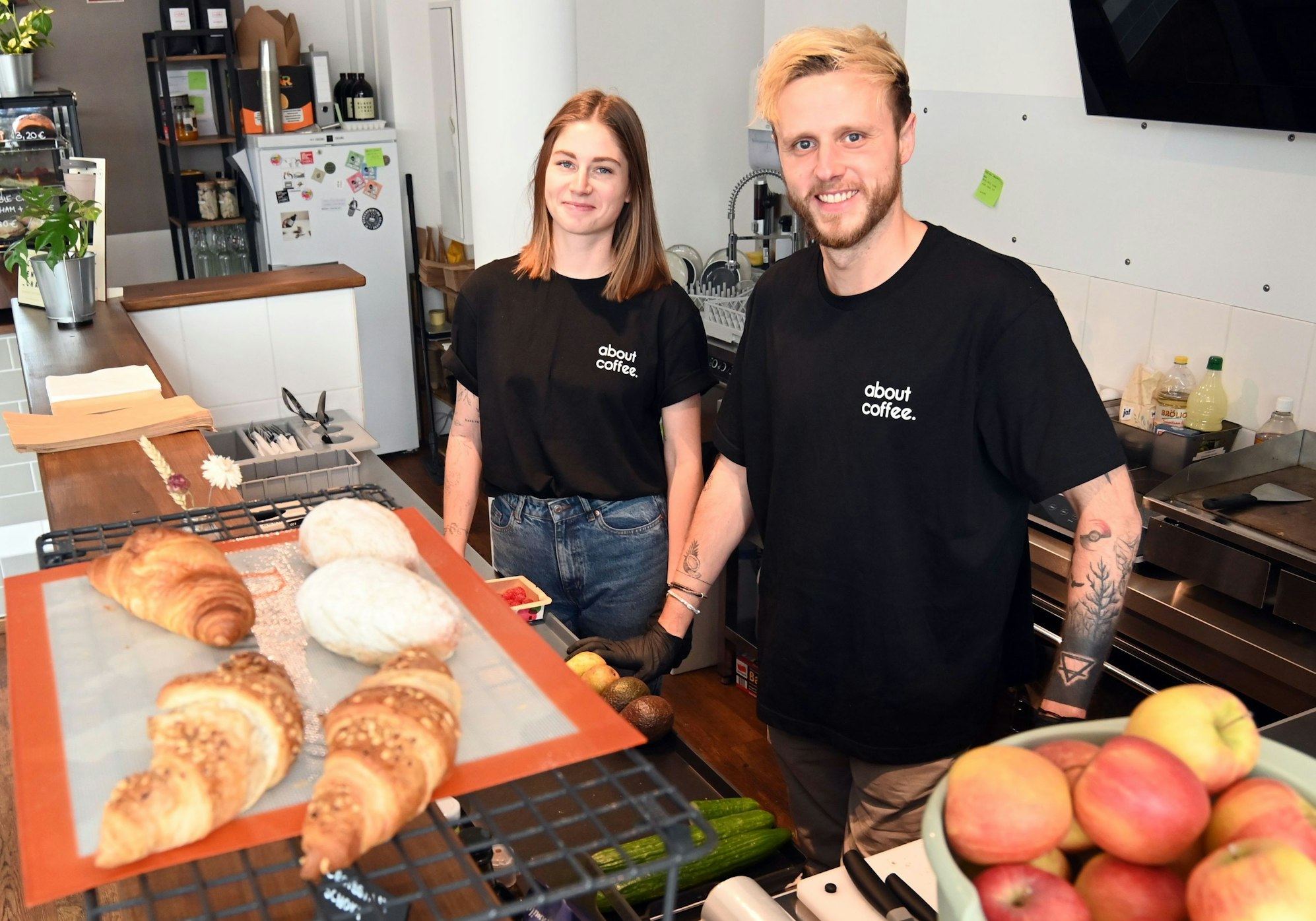 Mara und Patrick Gottschalk stehen hinter einer Theke, auf der Croissants stehen, und lachen in die Kamera