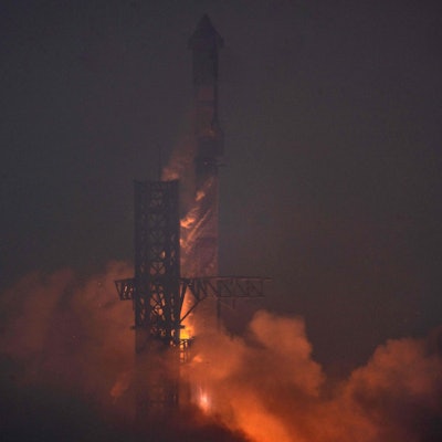 Im Dunkeln findet ein Raketenstart statt, dessen Antrieb die entstehende Rauchentwicklung beleuchtet.