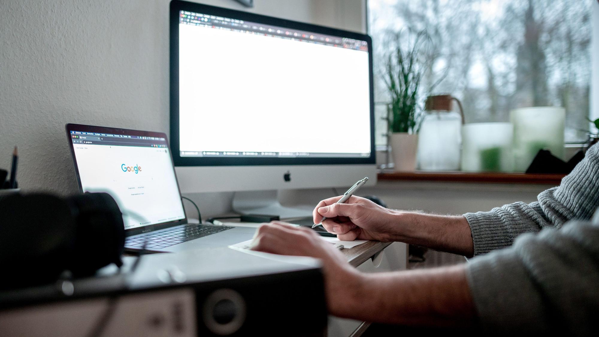 Ein Mann arbeitet im Home Office, vor ihm steht ein Laptop und ein großer Bildschirm.