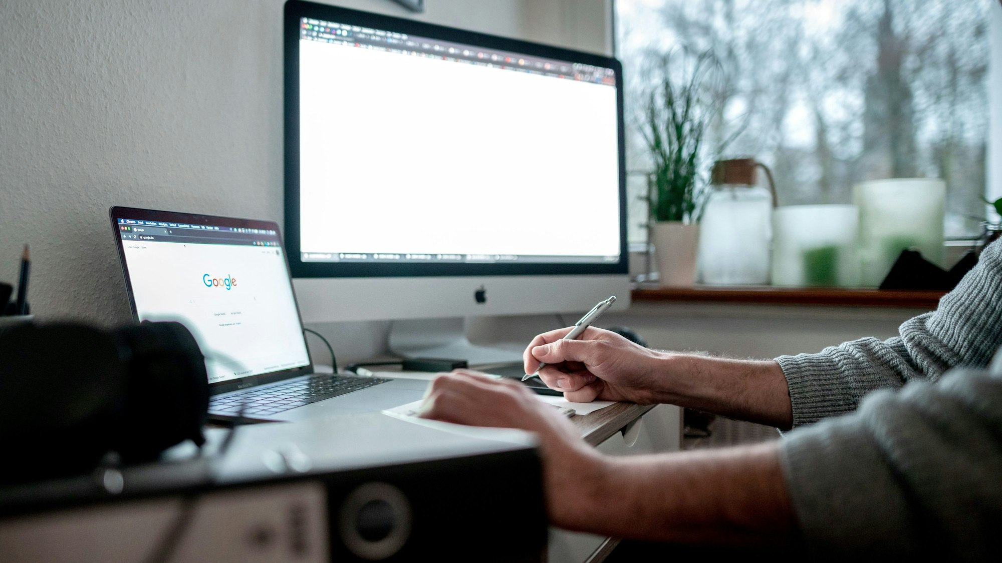 Ein Mann arbeitet im Home Office, vor ihm steht ein Laptop und ein großer Bildschirm.
