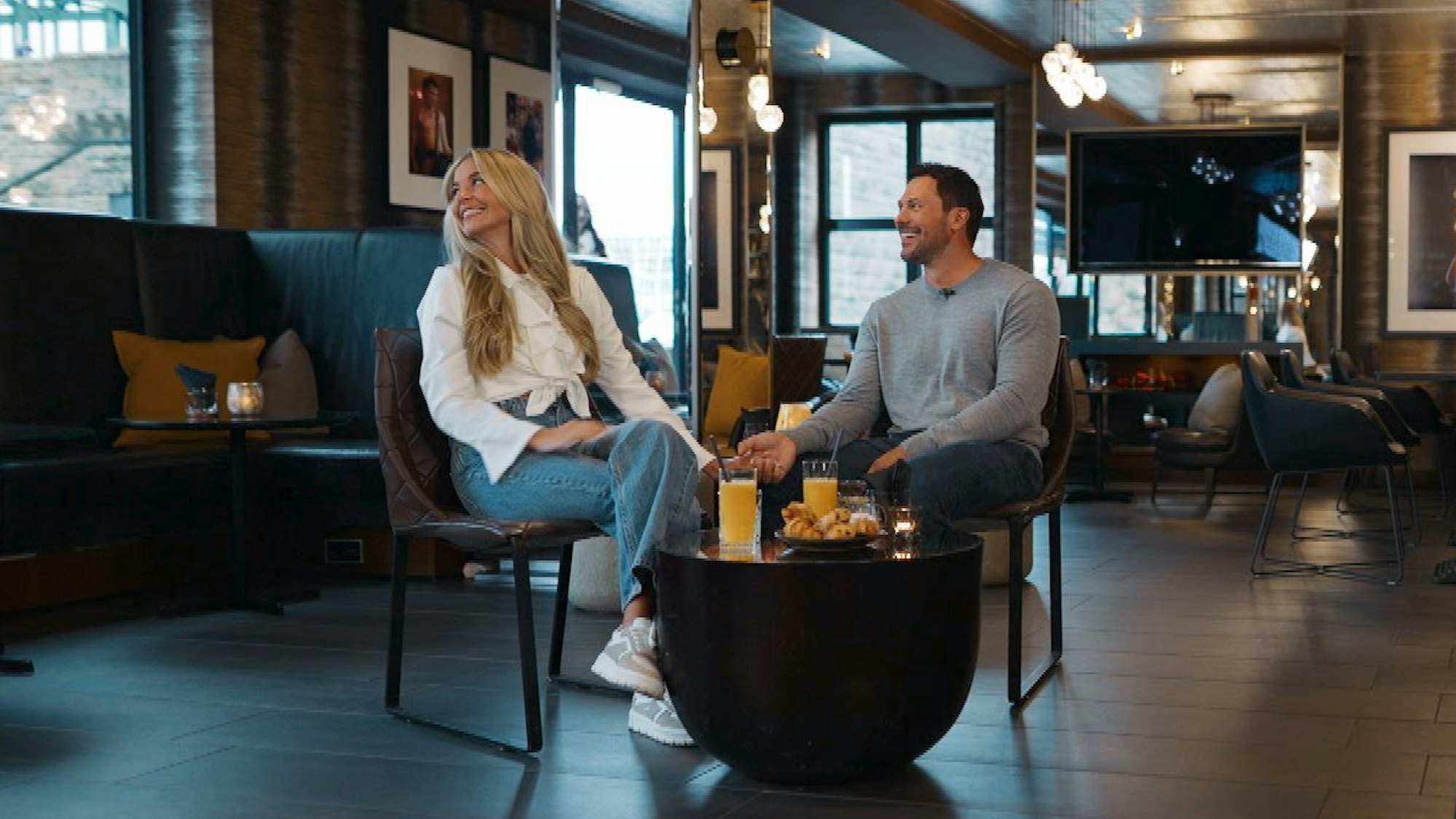 Eine Frau und ein Mann sitzen auf zwei Stühlen. Vor ihnen ein Tisch mit Säften und Gebäck.