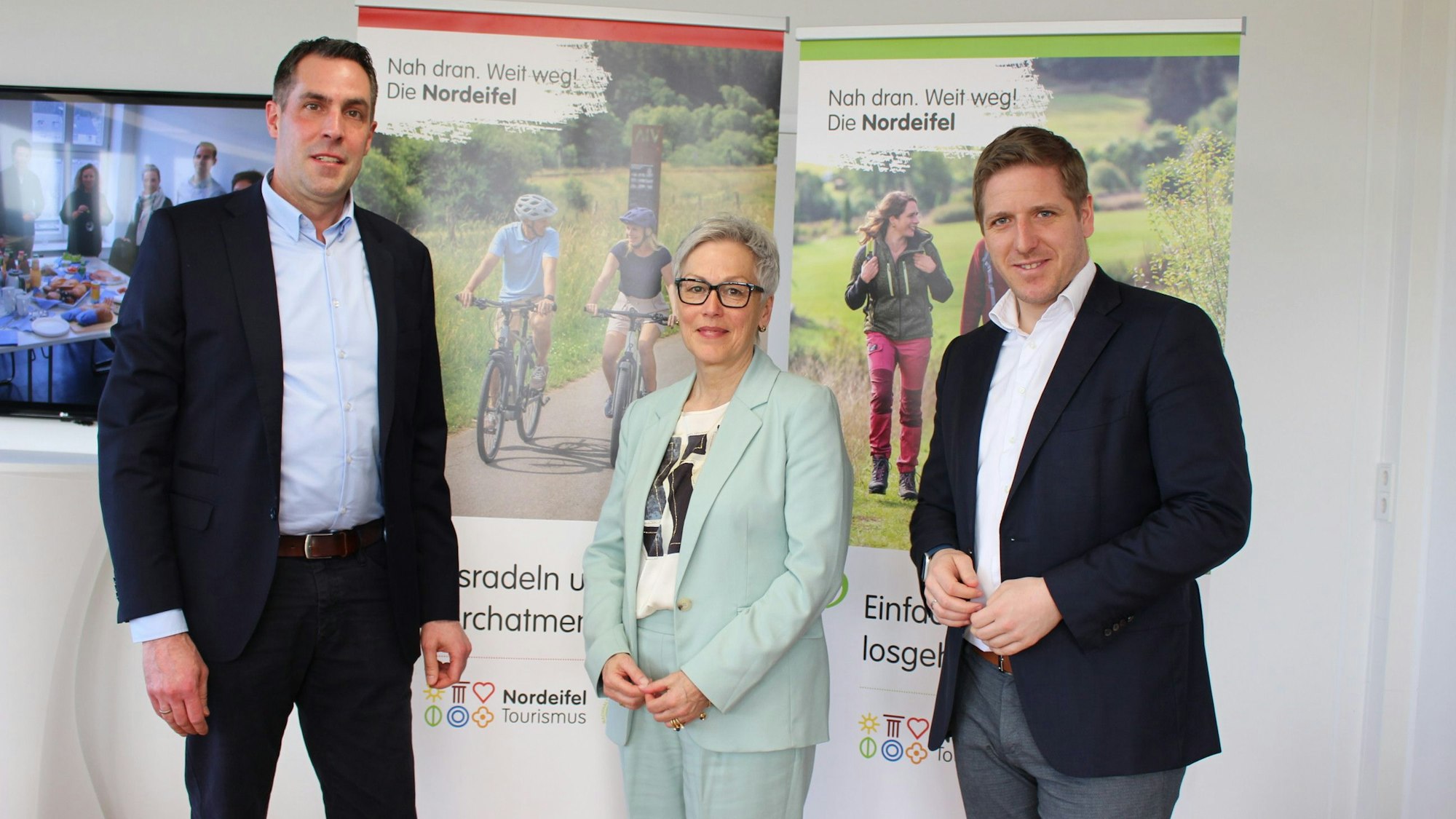Patrick Schmidder (l.), Iris Poth und Markus Ramers stehen vor Plakaten der Nordeifel Tourismus GmbH.