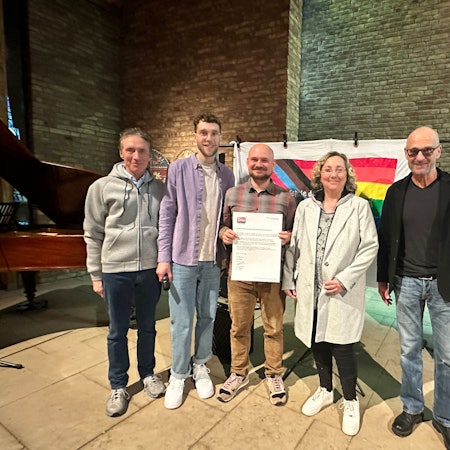 Vier Männer und eine Frau stehen nebeneinander, einer hält einen Vertrag in der Hand, der überdimensioniert groß ist.