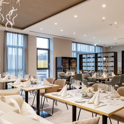 Zu sehen ist ein helles Restaurant mit gedeckten Tischen und Weinregalen.