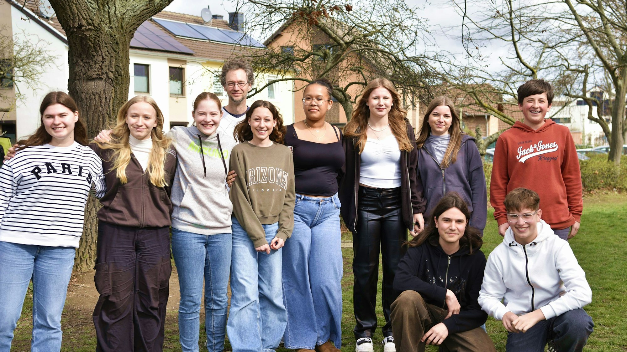 Zehn Jugendliche stehen mit ihrem Lehrer auf einer Wiese.