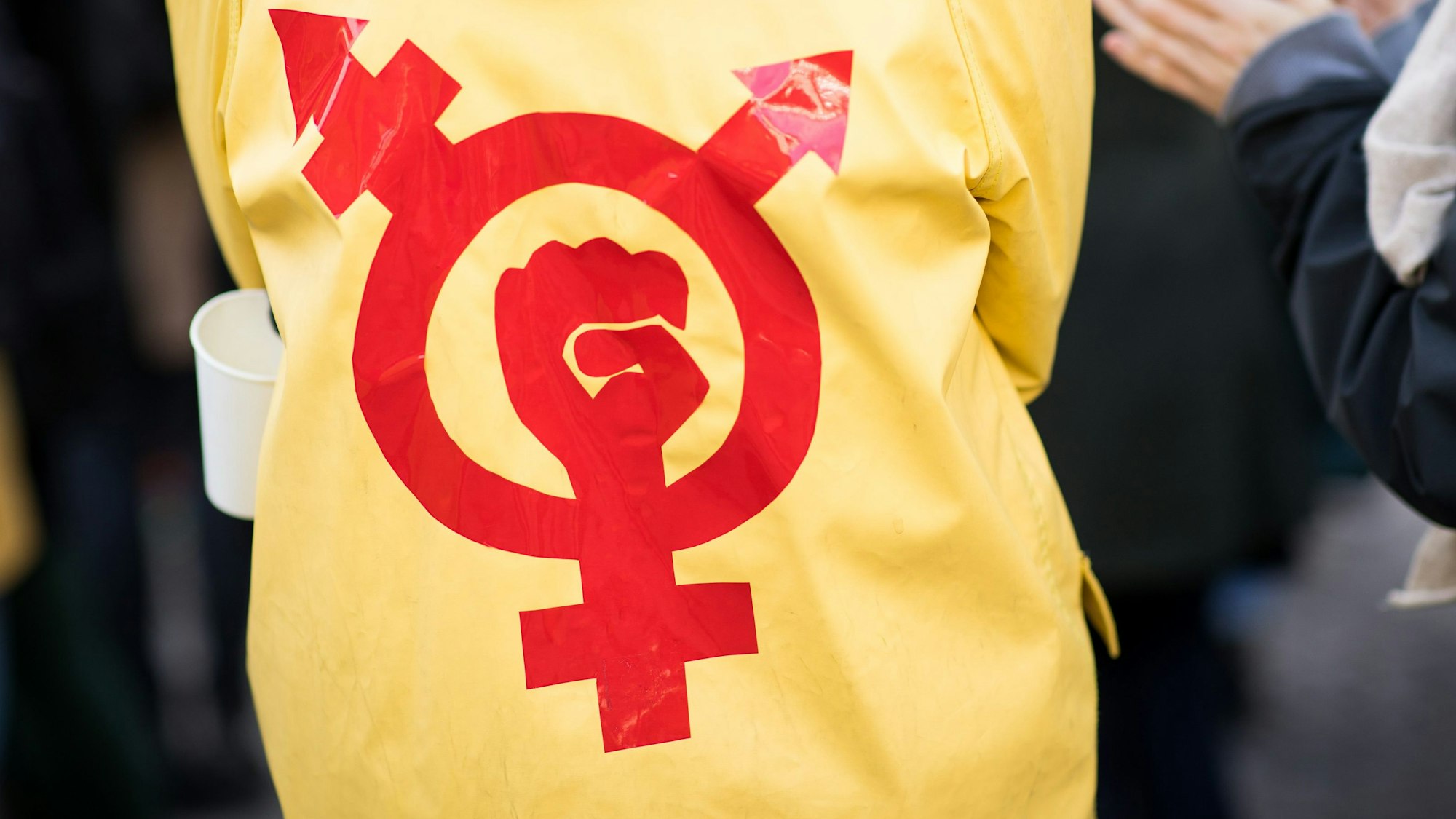 Eine Frau trägt einen gelben Regenmantel mit einem Gender- und Protestsymbol bei einer Kundgebung zum Internationalen Frauentag vor dem Rathaus in Hamburg.