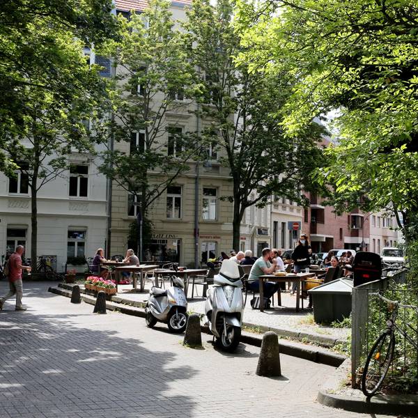 Blick auf einen etwas erhöhten Platz, auf Tische und Stühle eines Cafés stehen