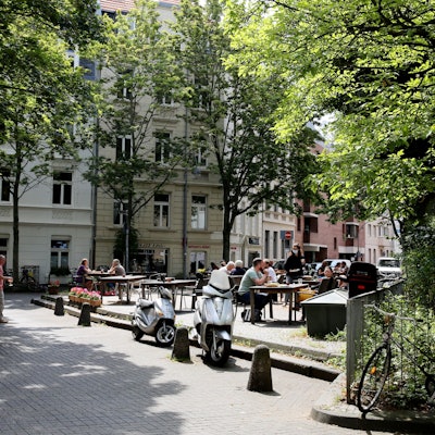 Blick auf einen etwas erhöhten Platz, auf Tische und Stühle eines Cafés stehen