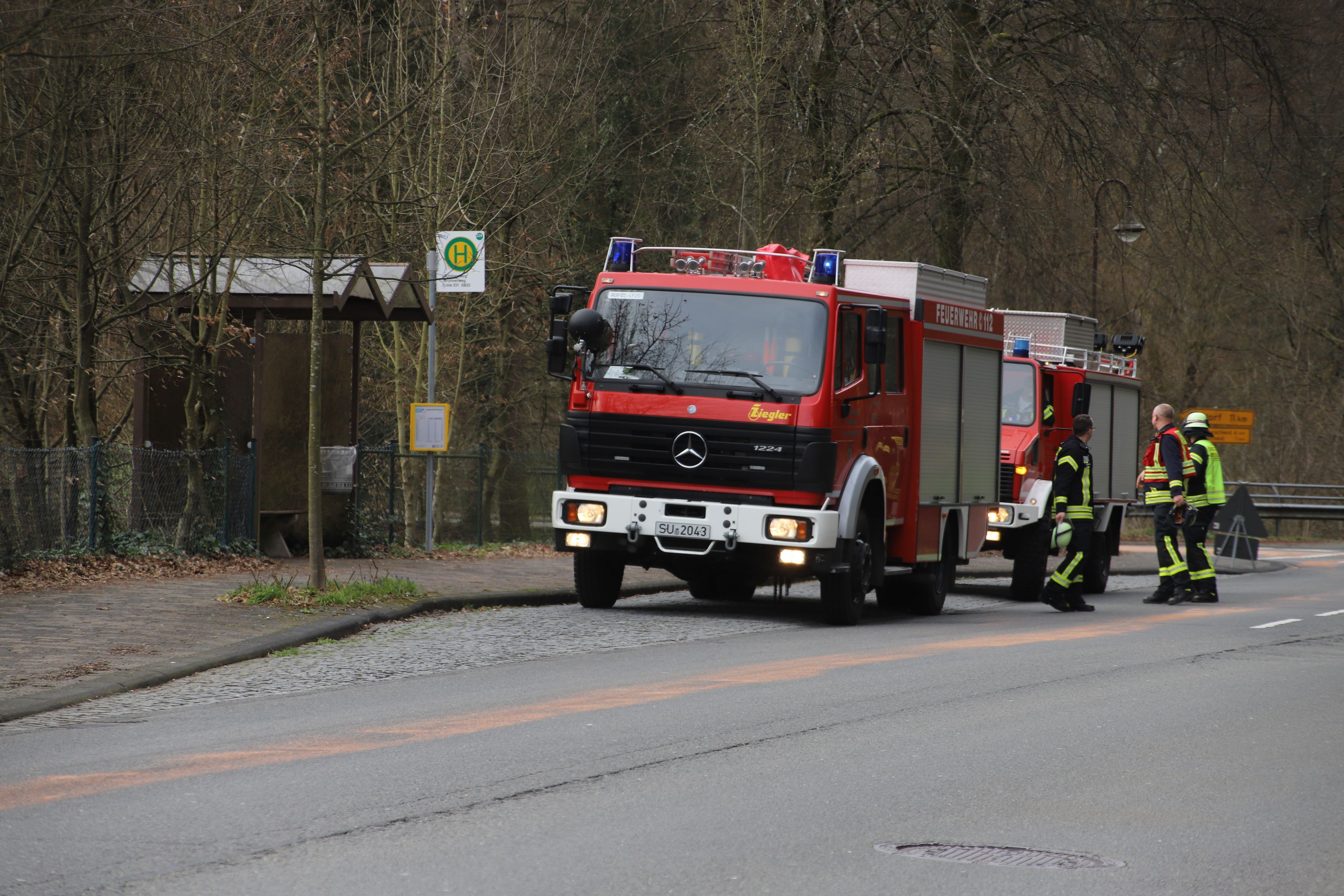 Feuerwehrleute stehen neben zwei Einsatzfahrzeugen der Feuerwehr.