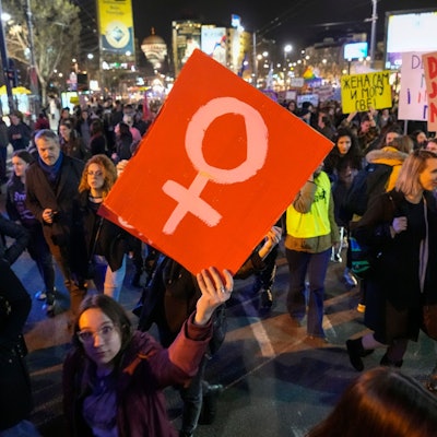 Das Bild zeigt eine demonstrierende Frau, die ein Schild in die Höhe reckt.