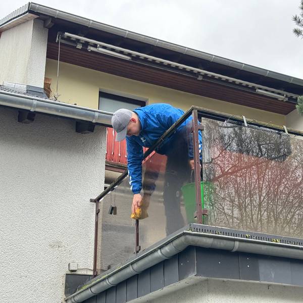 Ein Mann putzt die Brüstung eines Balkons mit einem Schwamm.