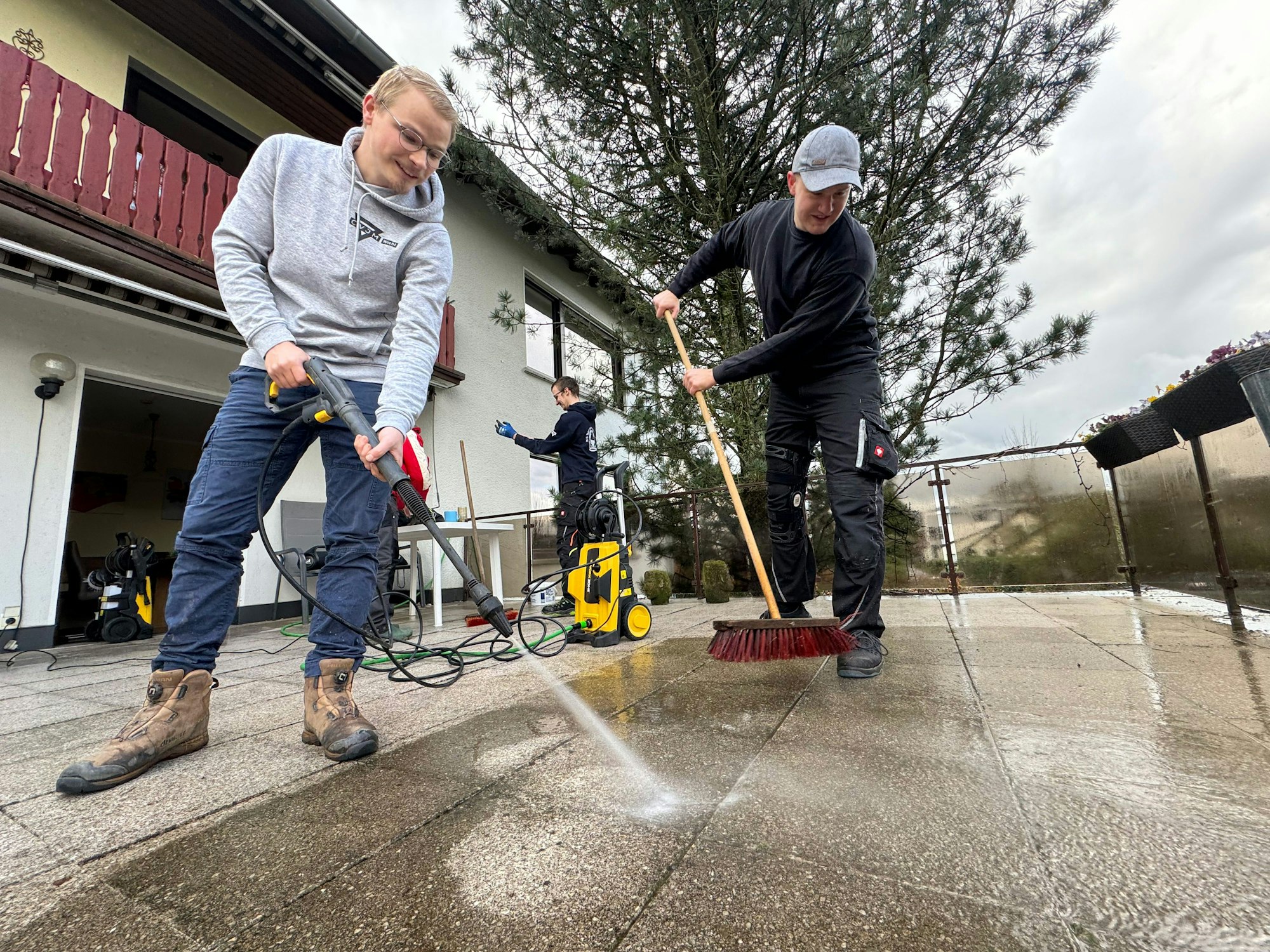 Ein Mann reinigt mit einem Hochdruckreiniger eine Terrasse.