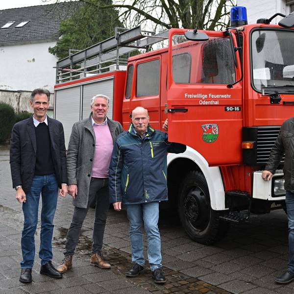 Ein Löschfahrzeug der Feuerwehr, davor vier Männer.