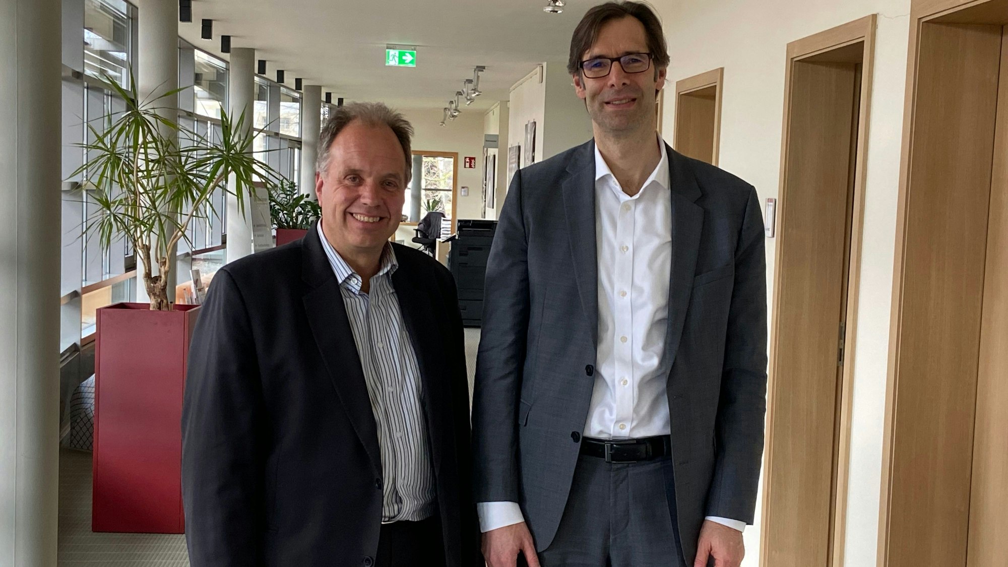Zwei Männer stehen nebeneinander in einem Gebäudeflur.